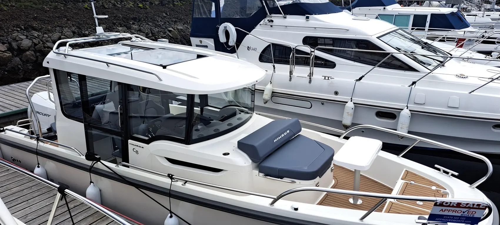 A Nimbus C8 boat docked with a grey cushion and a table, features a "FOR SALE" sign in a marina.